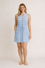 Woman wearing a light blue sleeveless dress with buttons on a plain background