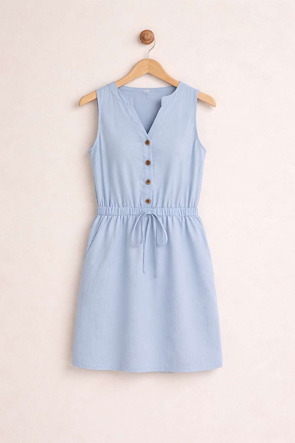 Light blue sleeveless dress with buttons on a beige background