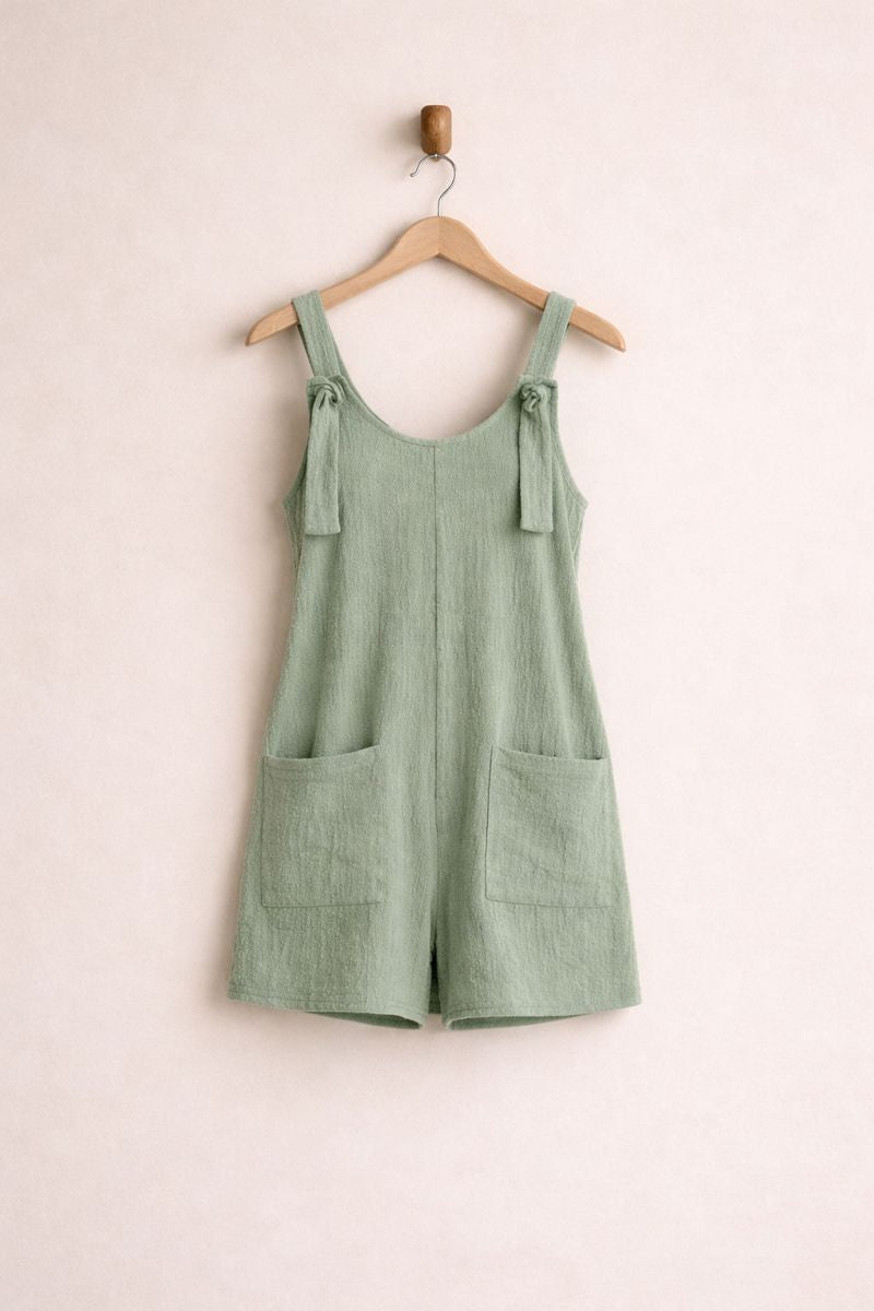 Green overalls hanging on a wooden hanger against a light pink background