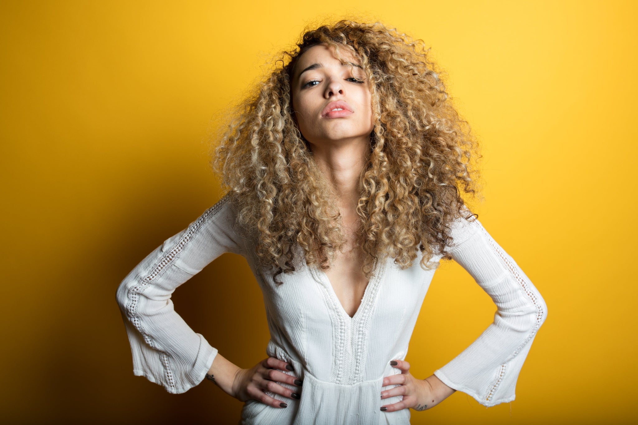 Woman with curly hair wearing a white dress against a yellow background