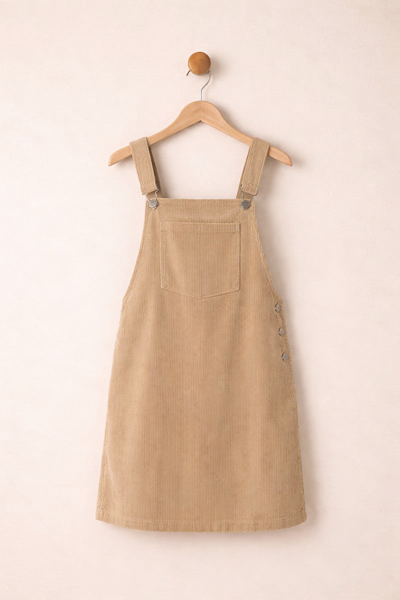 Beige corduroy pinafore dress on a wooden hanger against a beige background