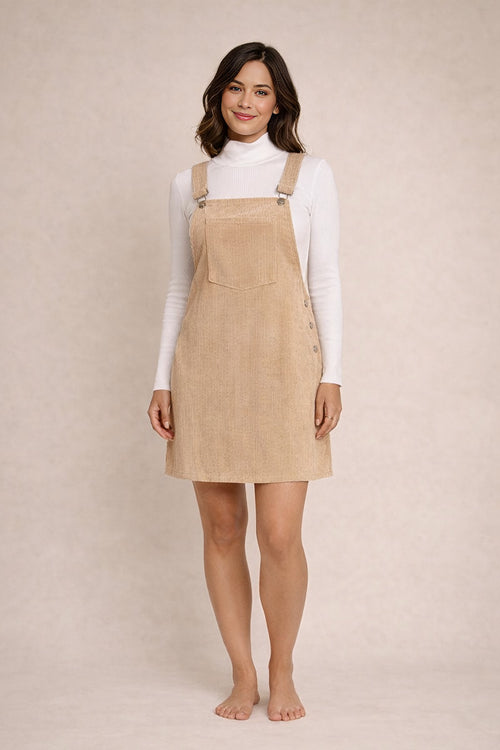 Woman wearing a beige pinafore dress over a white turtleneck on a beige background
