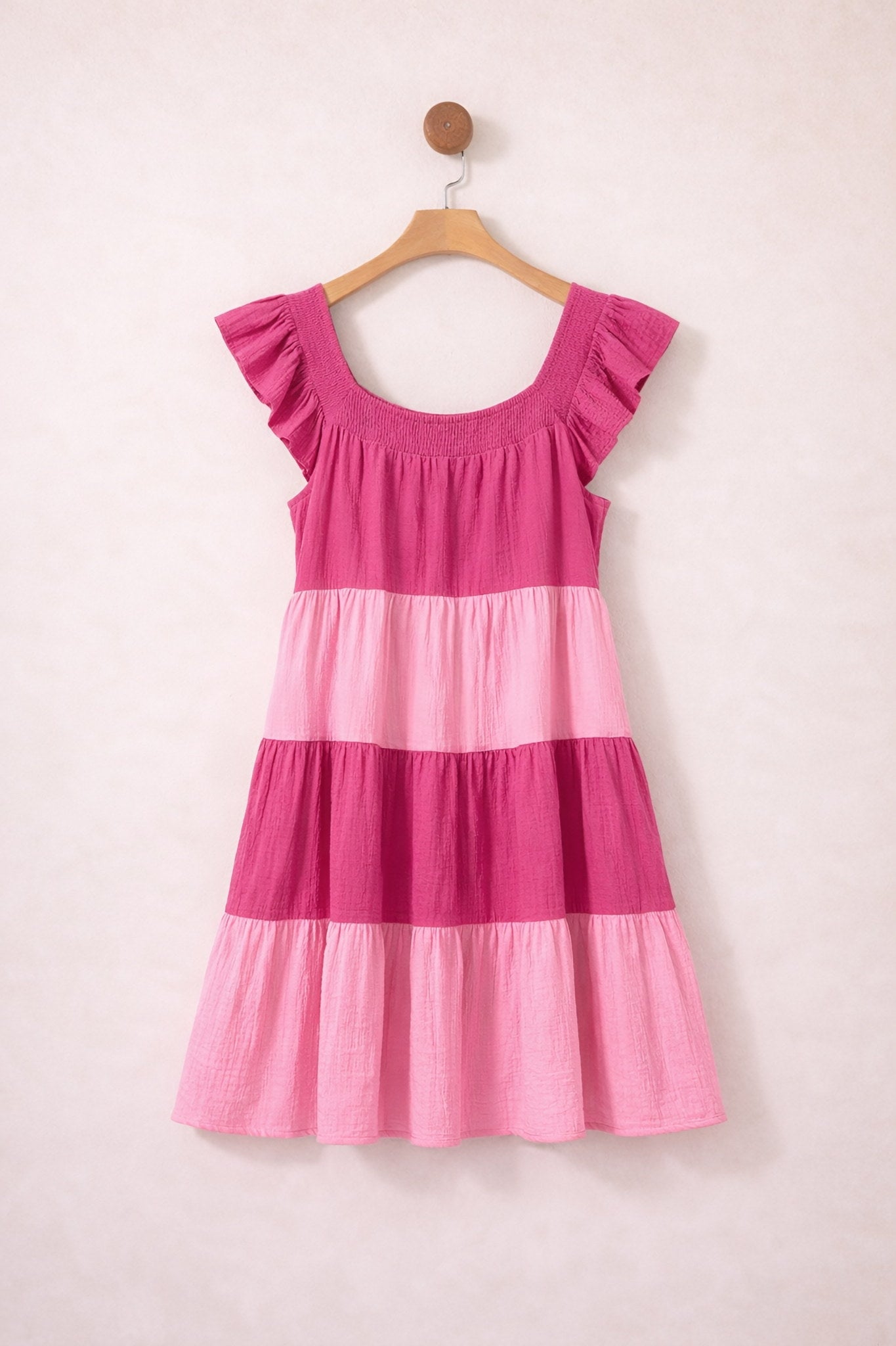 Pink and magenta striped dress on a hanger against a light pink background
