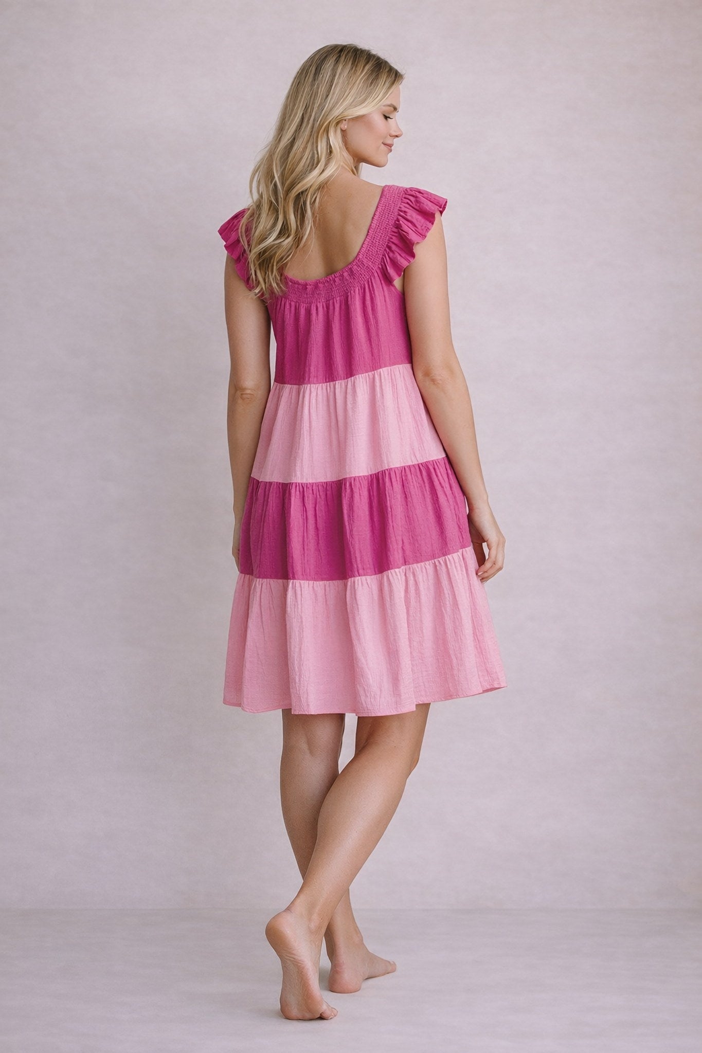 Woman wearing a pink and magenta tiered dress against a plain background