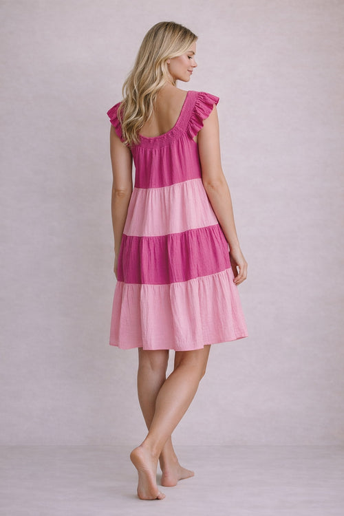 Woman wearing a pink and magenta tiered dress against a plain background