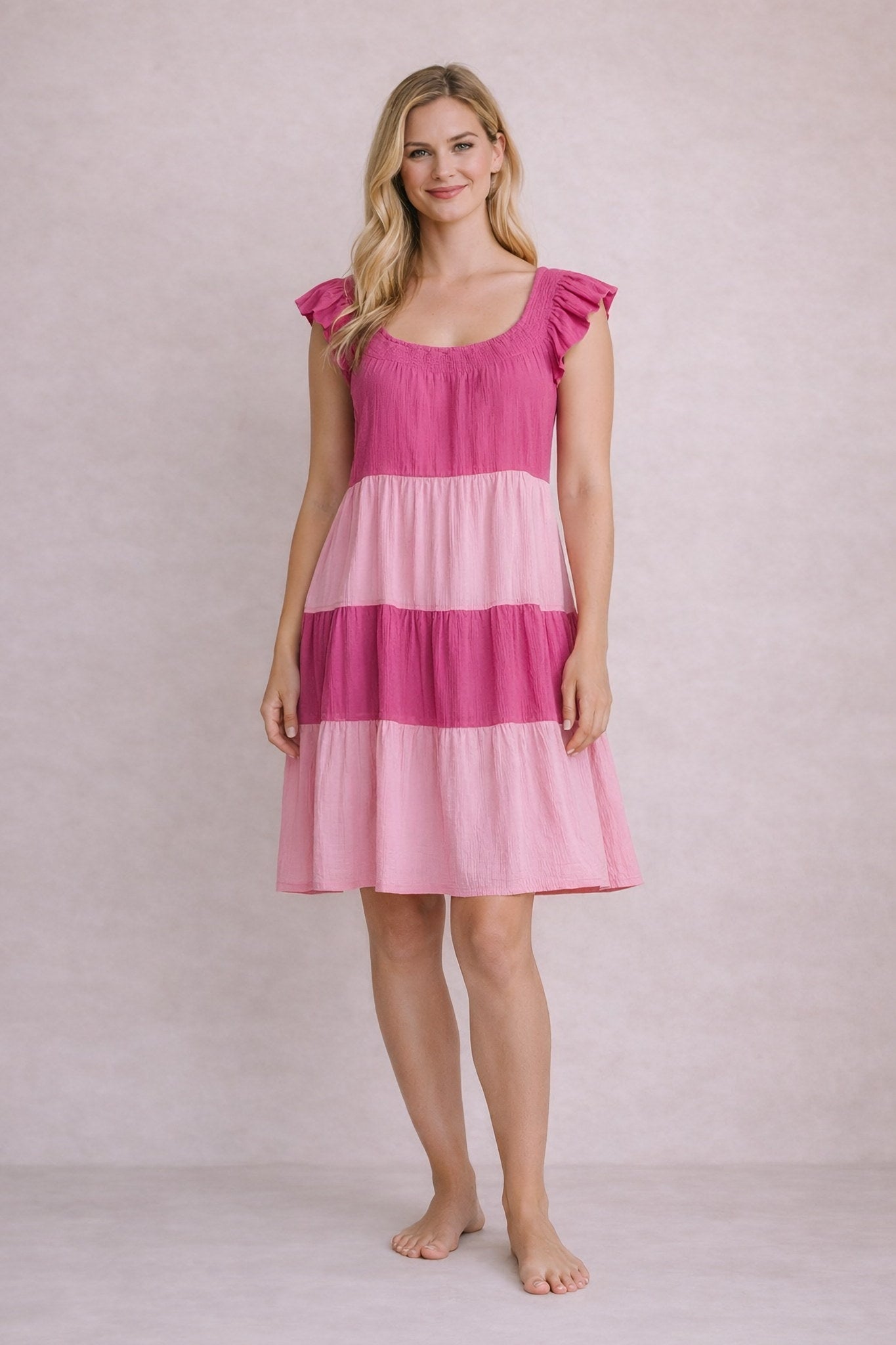 Woman wearing a pink and red tiered dress against a plain background