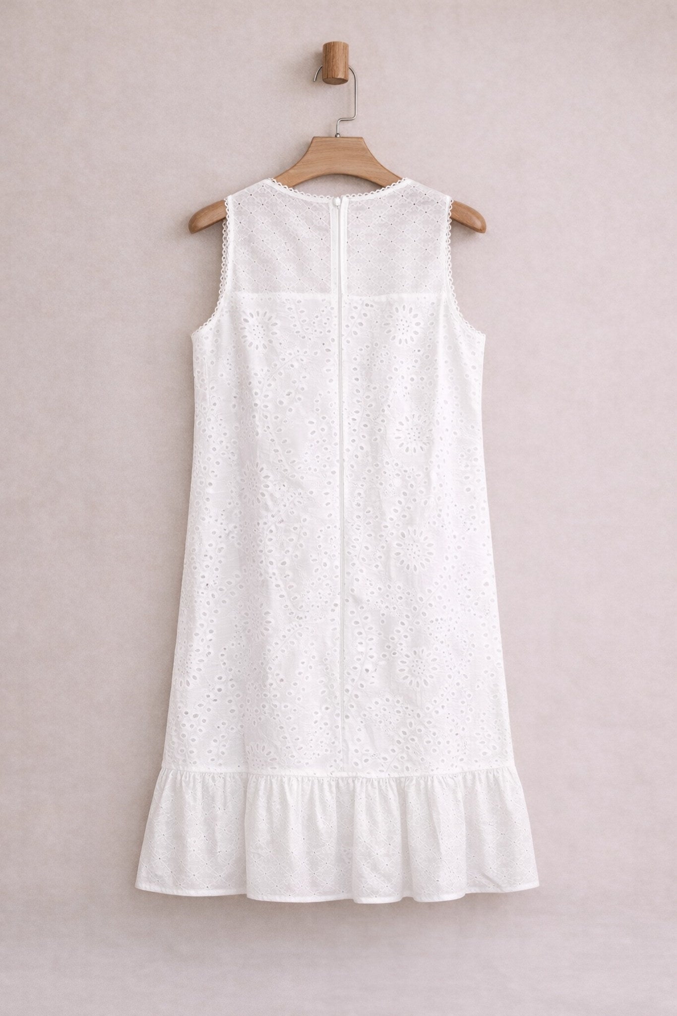 White sleeveless dress on a wooden hanger against a light pink background