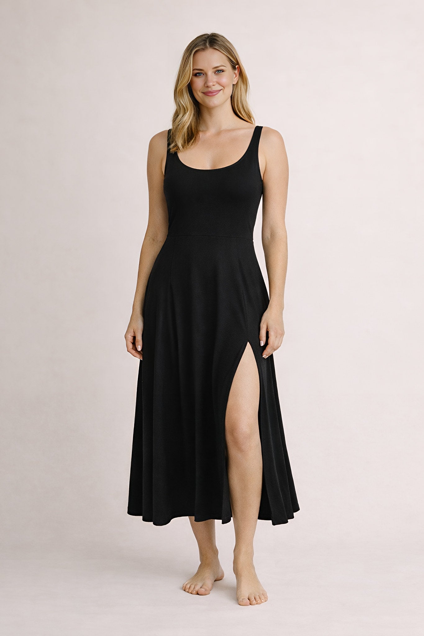 Woman wearing a black sleeveless dress with a slit on a plain background