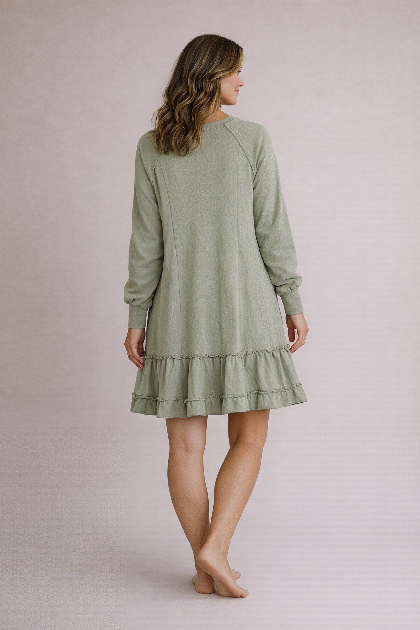 Woman wearing a green dress with long sleeves and a ruffled hem on a plain background