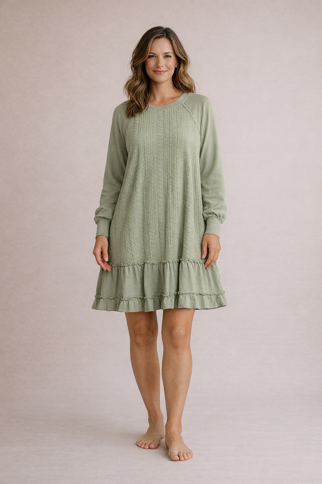 Woman wearing a green dress with long sleeves and ruffled hem on a plain background