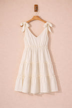 White dress with ruffled layers on a wooden hanger against a pink background