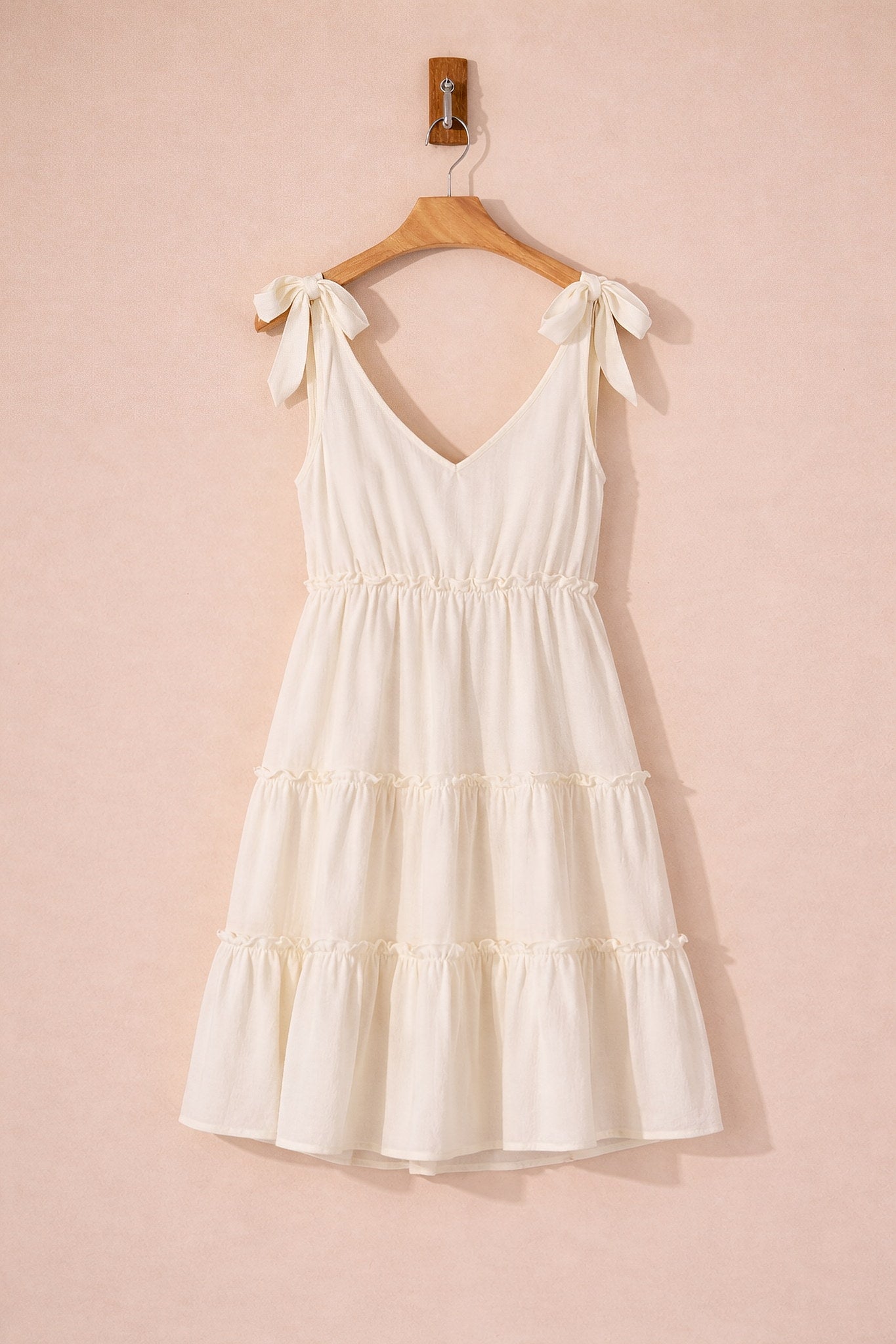 White dress with ruffled layers on a wooden hanger against a pink background