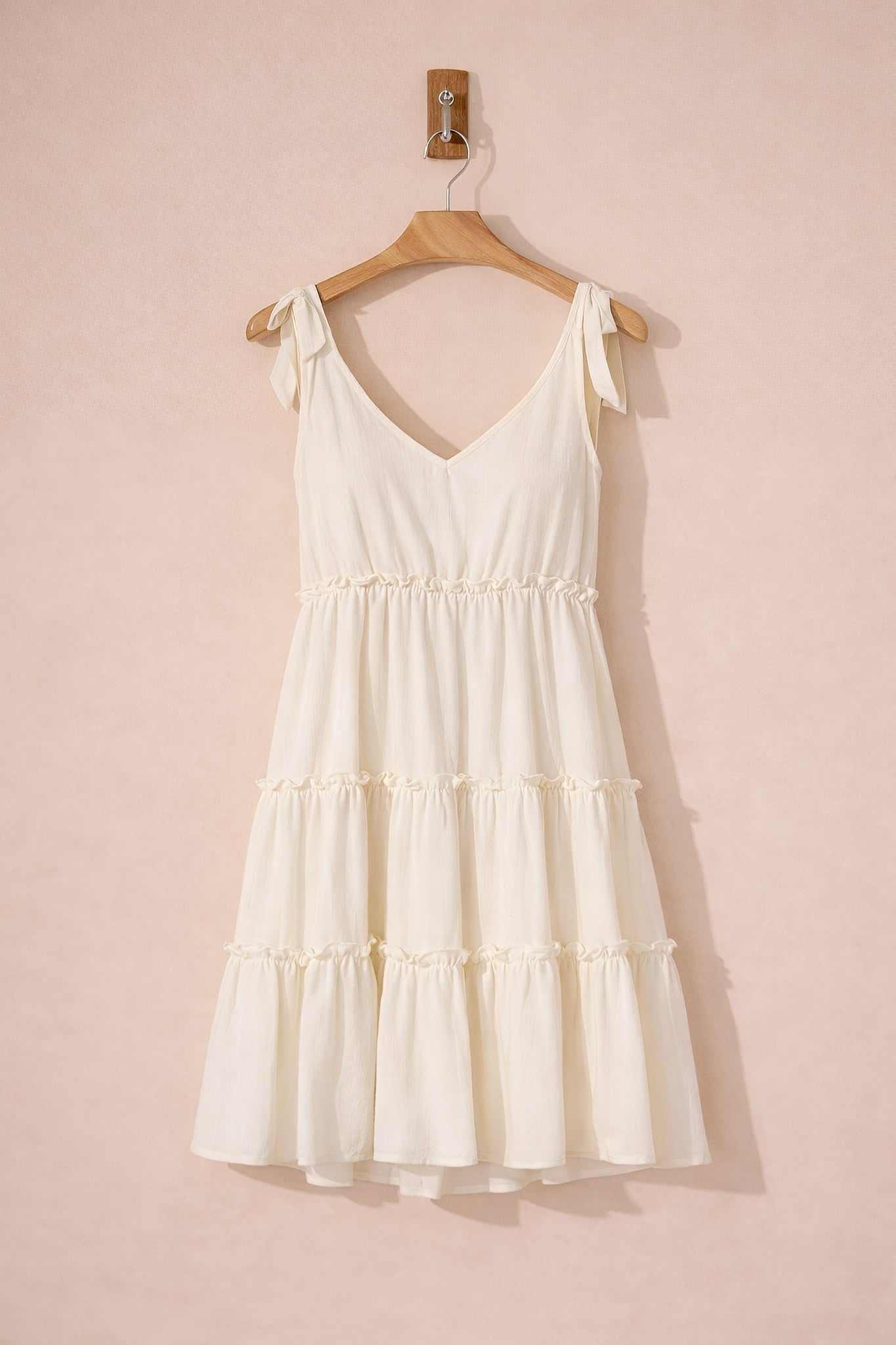 White dress on a wooden hanger against a pink background