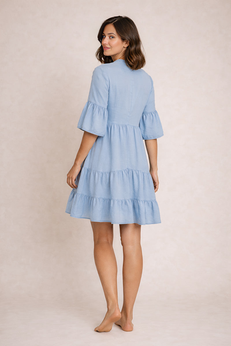 Woman wearing a light blue dress with ruffled sleeves and hem on a beige background