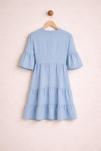 Light blue dress with ruffled sleeves and hem on a wooden hanger against a light pink background